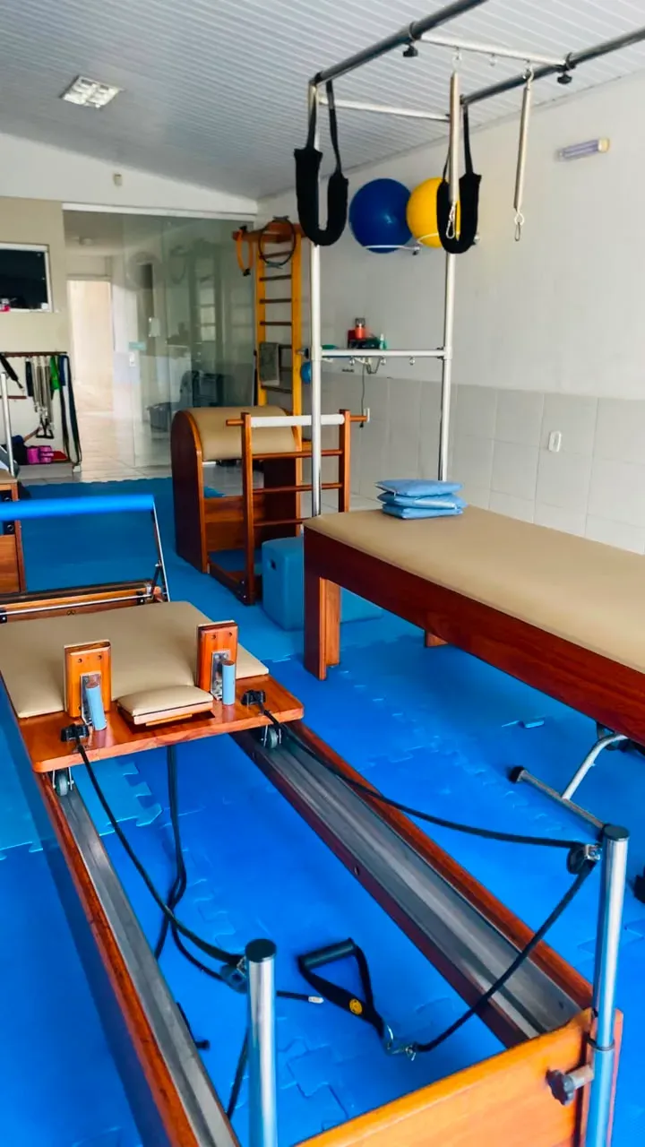 Estúdio de pilates com aparelhos de madeira e piso azul.