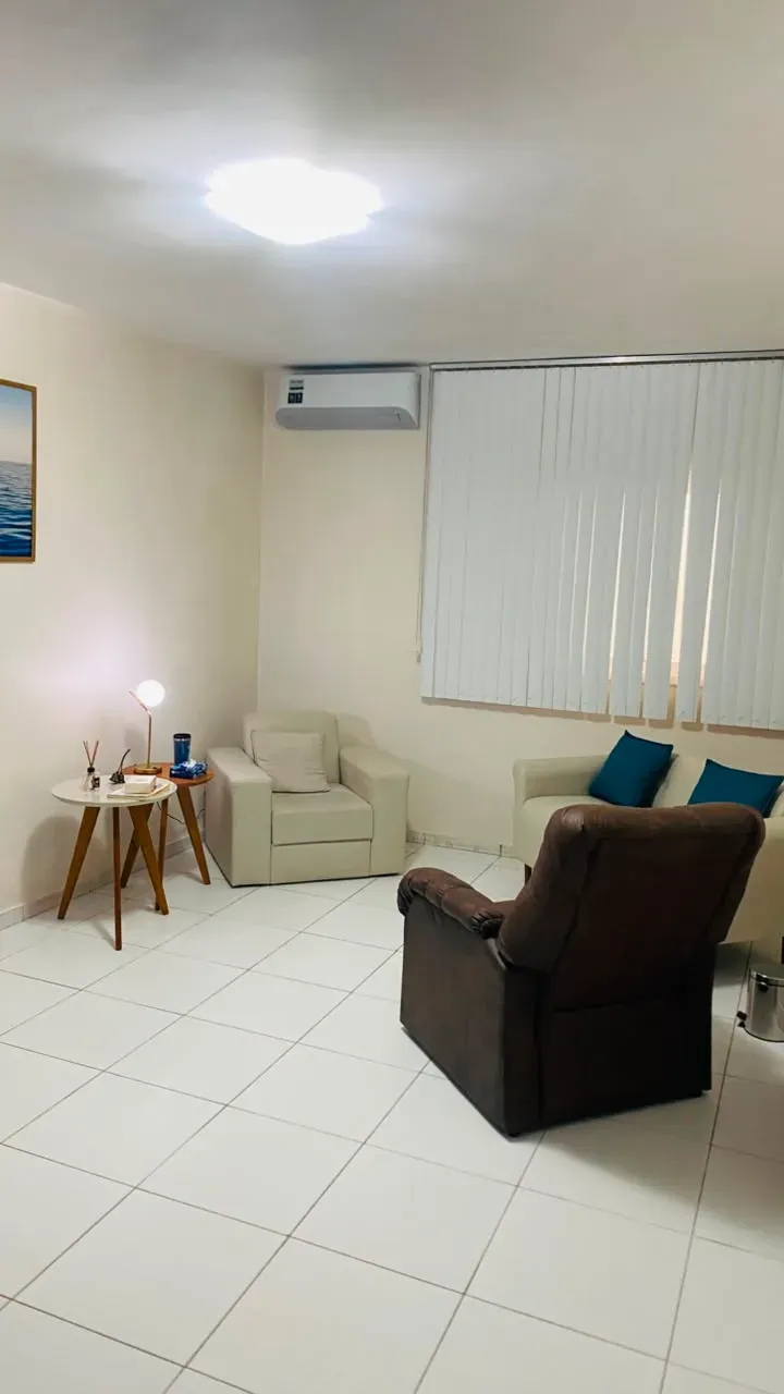 Sala de atendimento com poltronas, luminária de mesa, ar-condicionado e persiana.