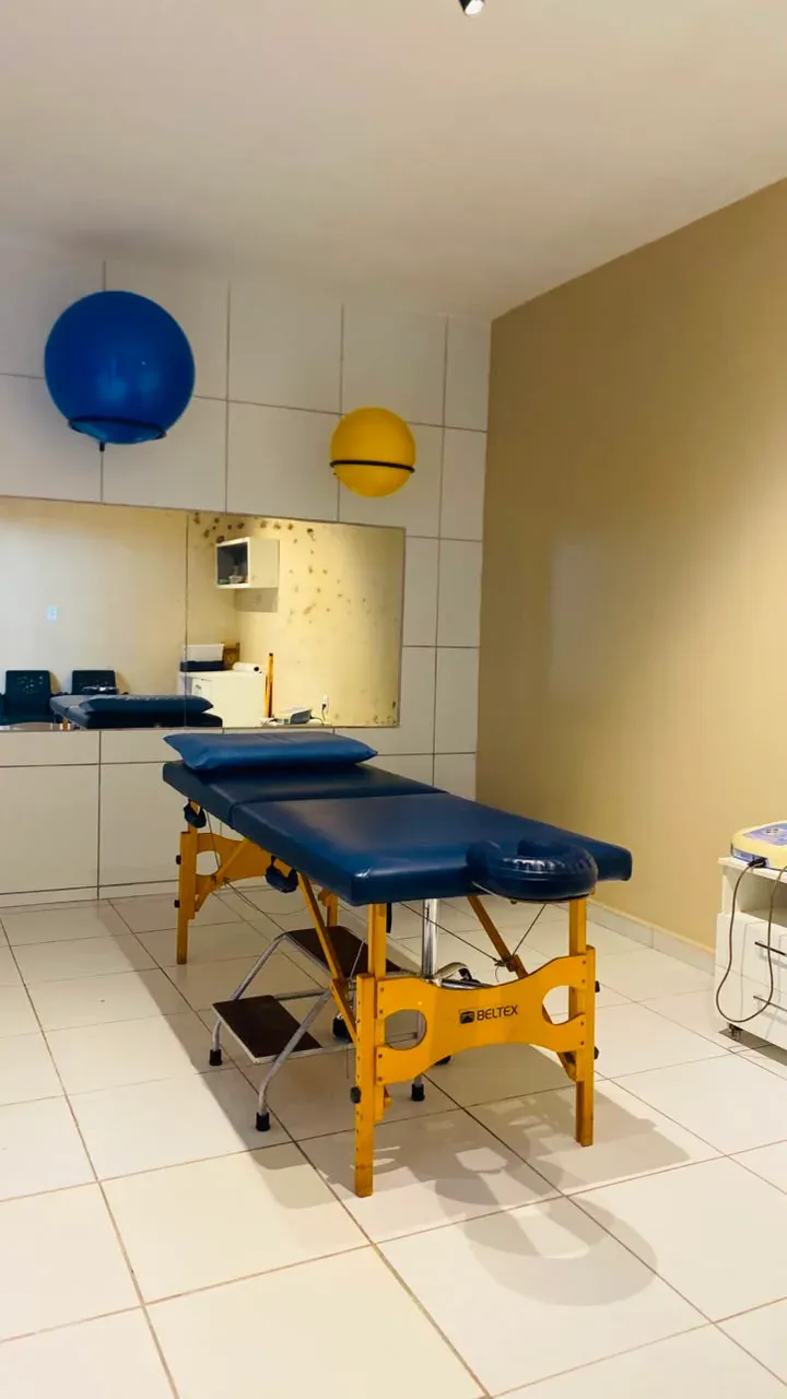 Sala de fisioterapia com maca azul, bolas de exercício e espelho.