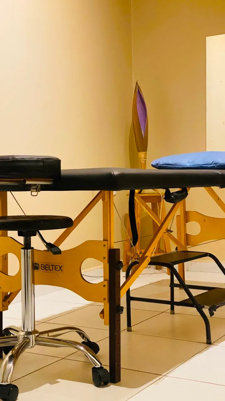 Sala de atendimento com maca preta, banqueta com rodízios e escada de apoio.